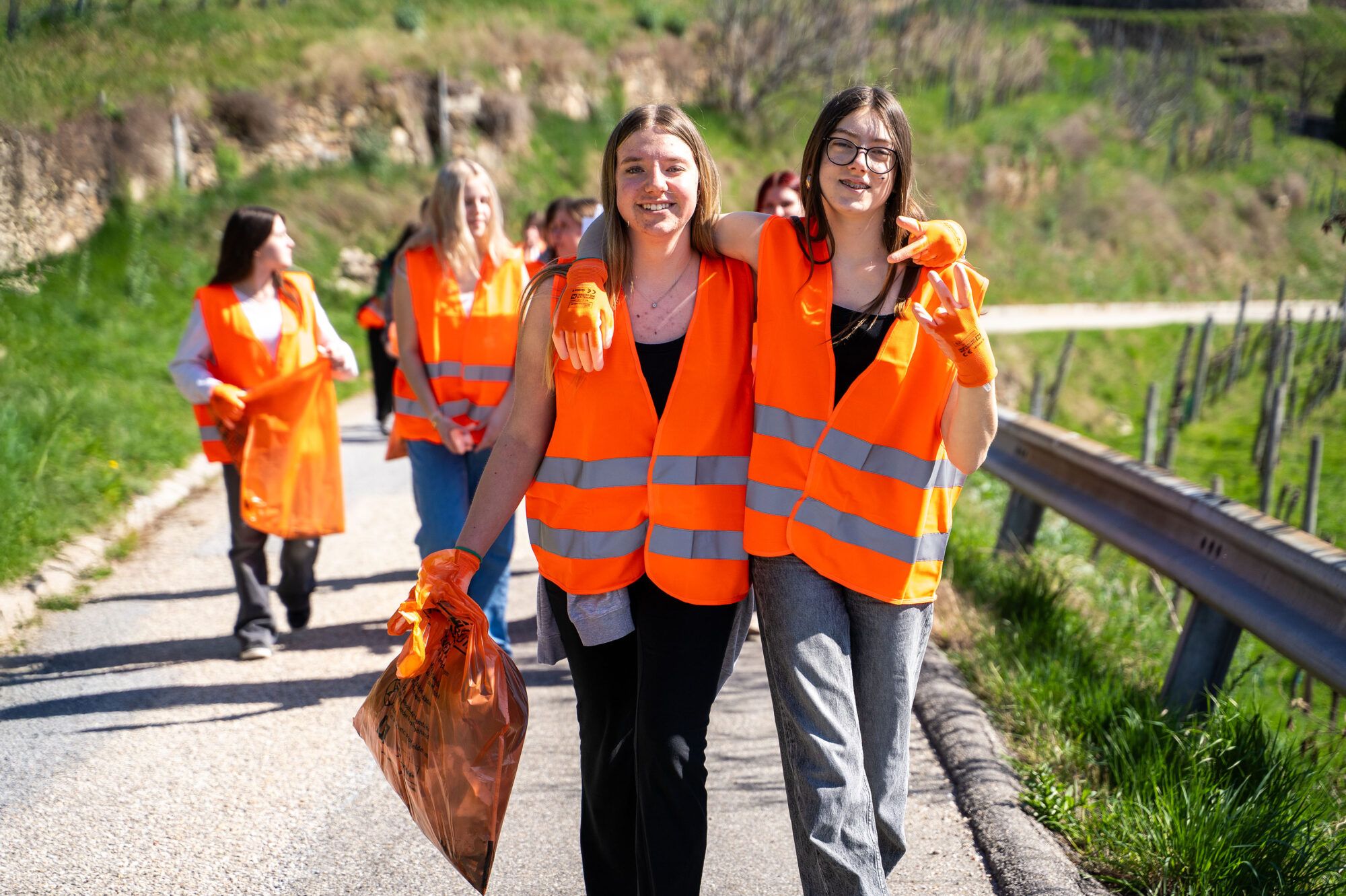 Gruppe Jugendliche in orangen Warnwesten, im Vordergrund 2 M&auml;dchen mit fr&ouml;hlichem Gesichtsausdruck