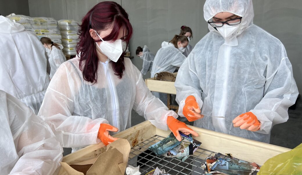 Eine Schülerin und ein Schüler, die Masken und Schutzanzüge tragen, sortieren den Abfall.