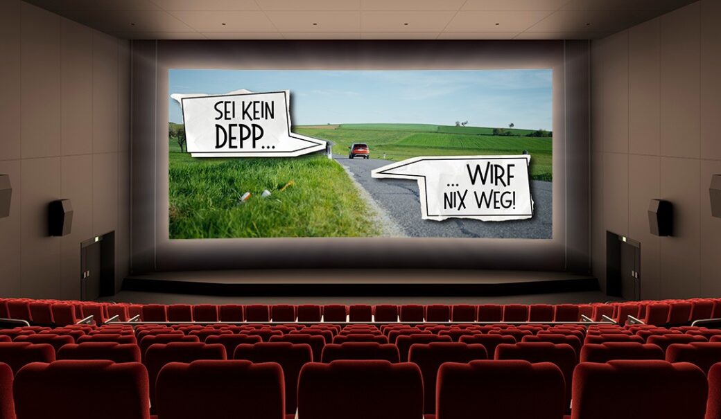 Kinosaal, auf der Kino-Leinwand sieht man einen Ausschnitt aus dem Werbespot auf dem eine Straße zu sehen ist mit einem Auto von hinten, seitlich liegt Abfall am Wegesrand und zwei große Sprechblasen sind zu sehen; in einer steht "Sei kein Depp...", in der anderen steht "Wirf nix weg!"